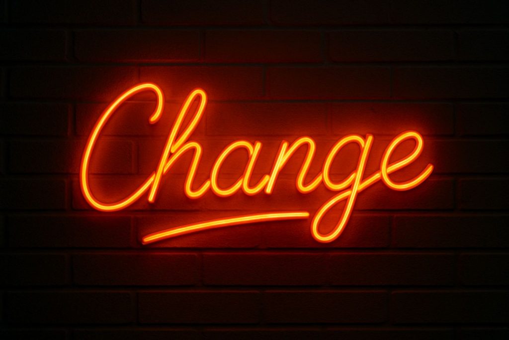 Neon sign spelling "Change" on a dark brick wall, symbolizing the theme to think the impossible and manage the change.