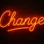 Neon sign spelling "Change" on a dark brick wall, symbolizing the theme to think the impossible and manage the change.