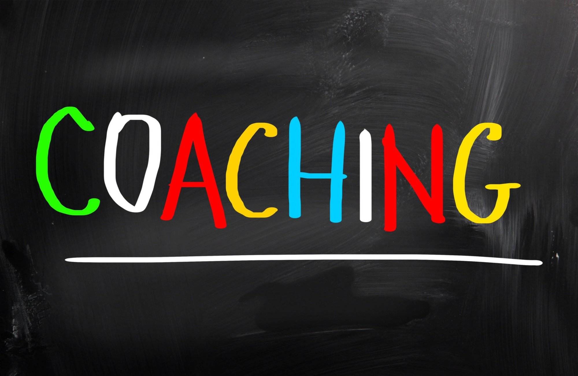COACHING" written in colorful letters on a black chalkboard background with a horizontal white line underneath.