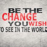 Man writing "Be the change you wish to see in the world" on a textured wall.