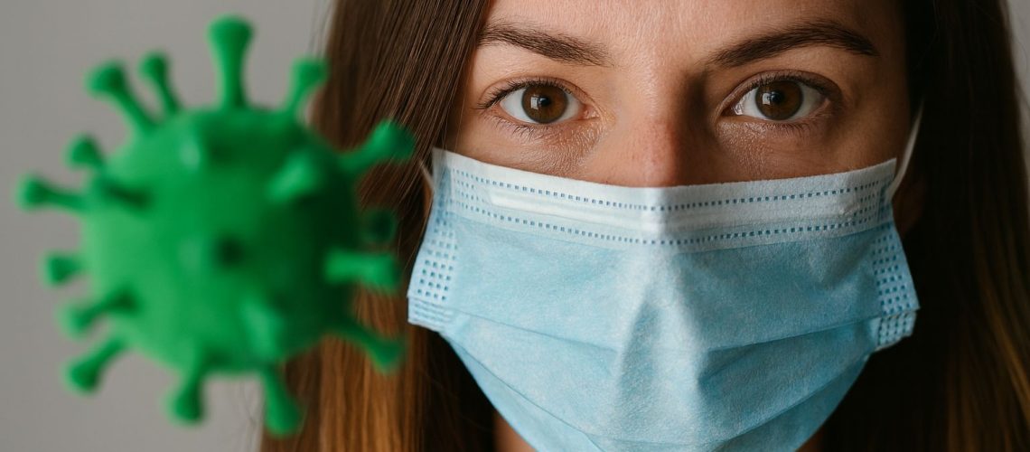 Woman wearing a mask looks at a green virus model, illustrating the impact of COVID-19 on the hierarchy of needs.