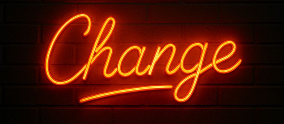 Neon sign spelling "Change" on a dark brick wall, symbolizing the theme to think the impossible and manage the change.